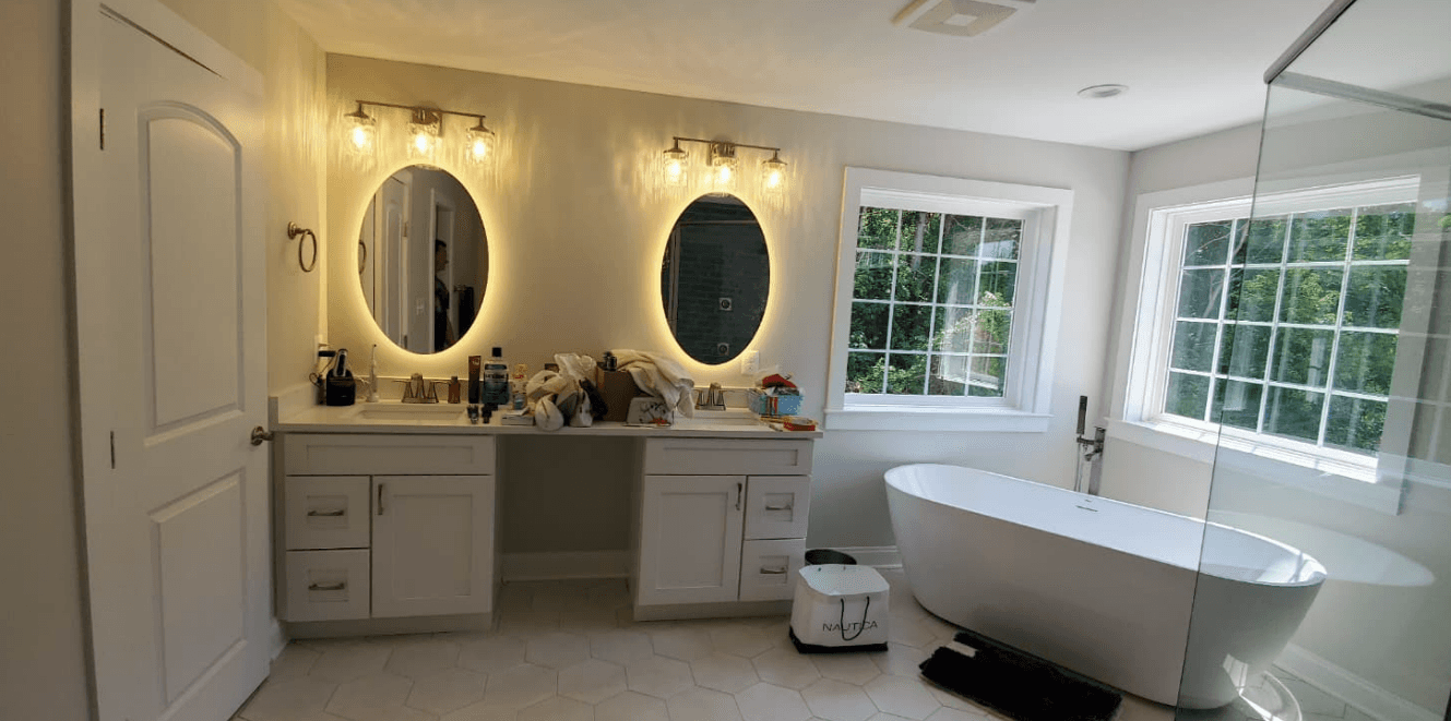 Modern bathroom with double vanity, backlit mirrors, and freestanding soaking tub with natural light