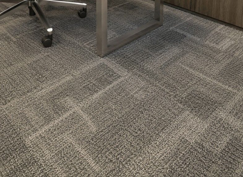 Close-up of gray Shaw commercial carpet tile pattern installed under office furniture and rolling chair wheels